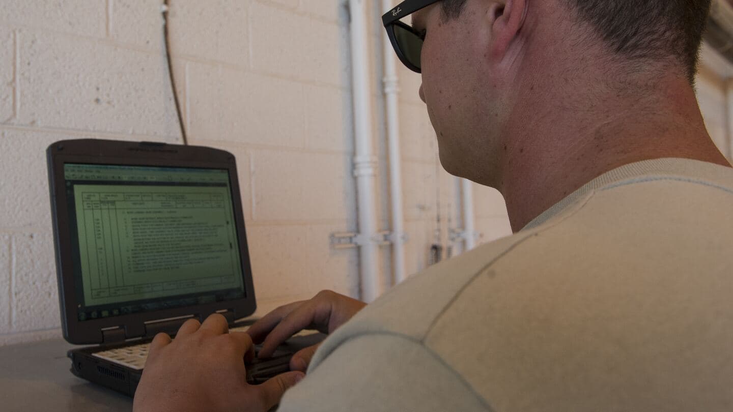 Over-the-shoulder view of an Airman reading a technical order on a rugged laptop