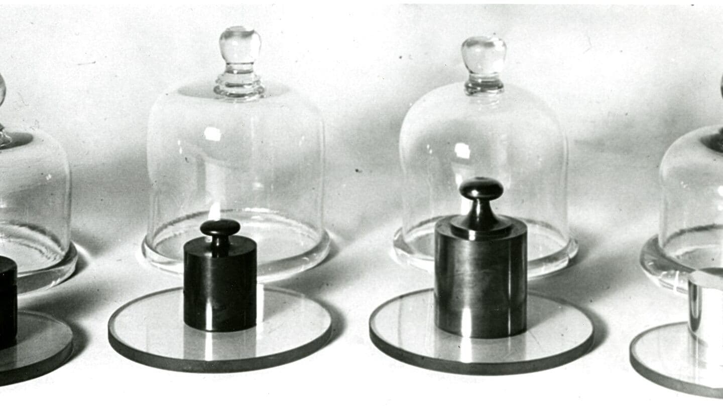 Four historical standard weights, each kept under its own glass bell jar