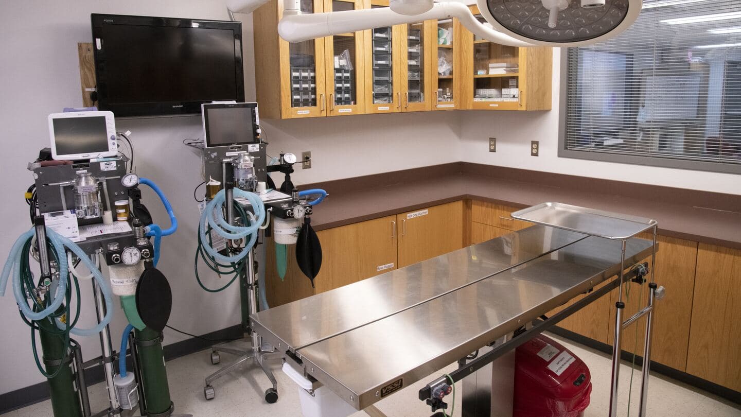A clinical procedure room with two identical anesthesia machines and patient monitors beside a steel table