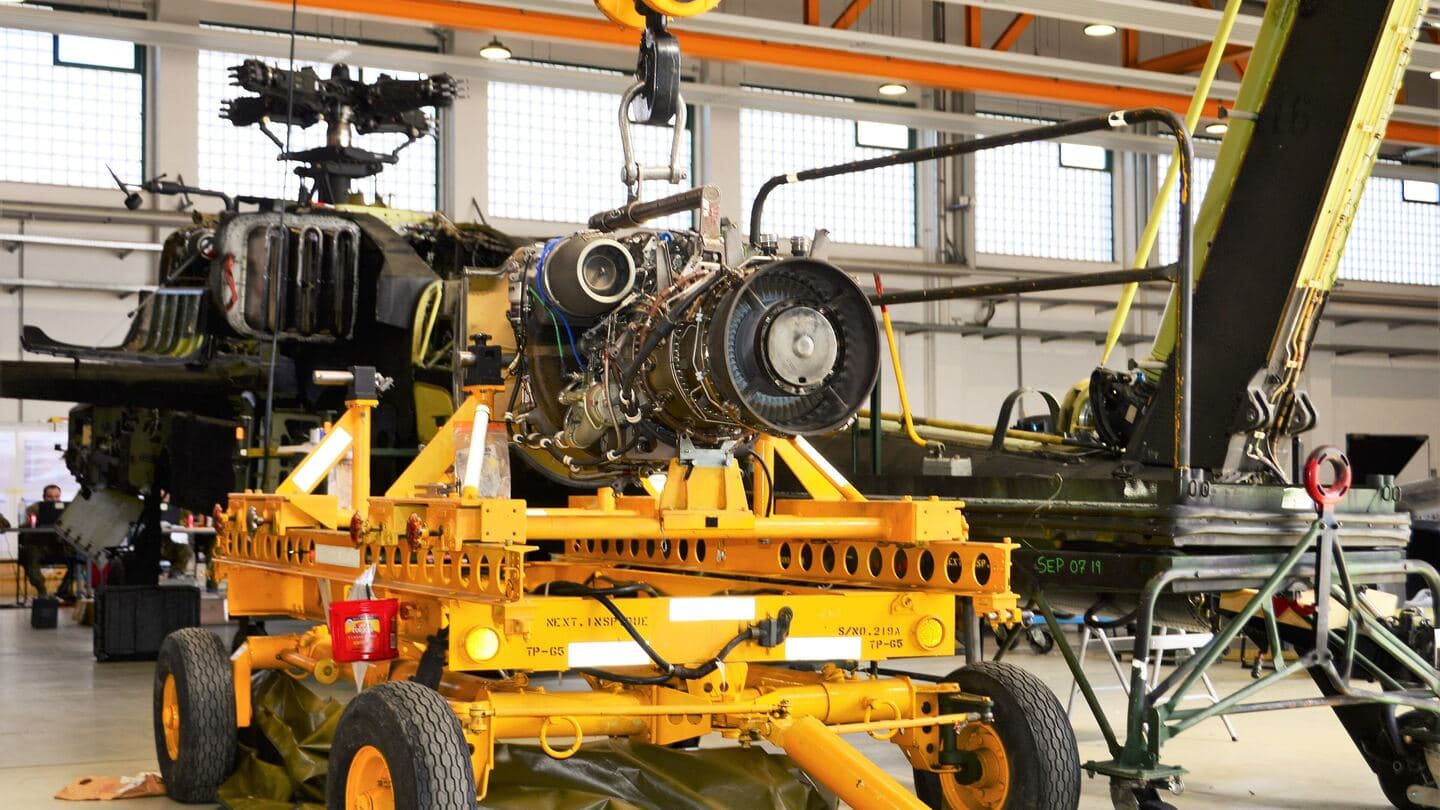 A helicopter turbine engine on a yellow maintenance stand beside a partly disassembled Apache