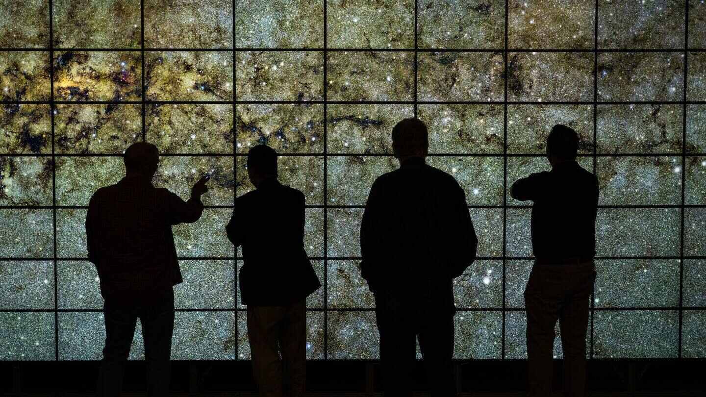 Silhouetted viewers in front of a wall of linked display screens