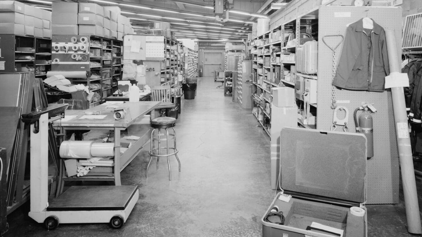 Black-and-white photo of a parts stockroom aisle at an airline maintenance hangar