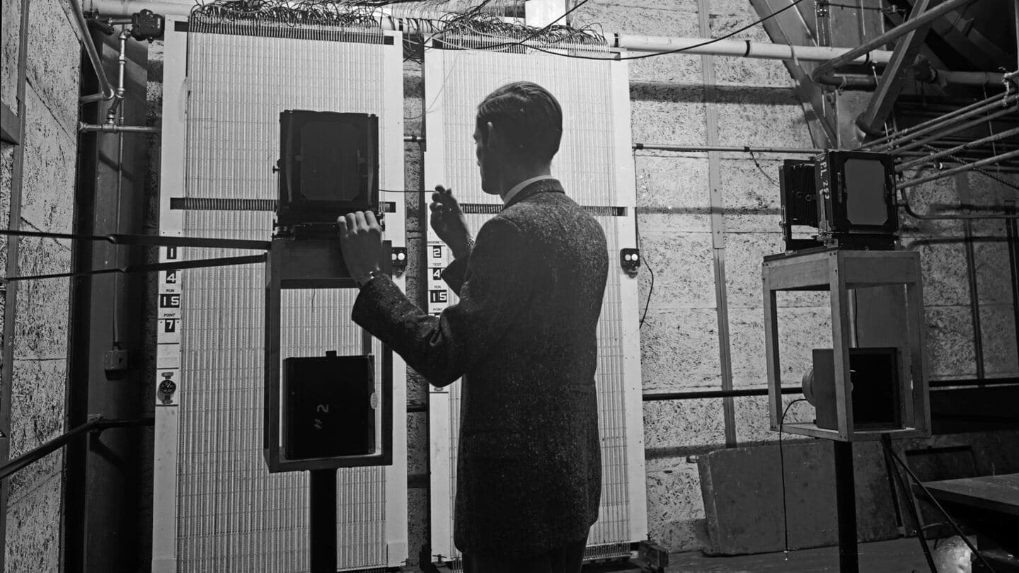 A technician seen from behind photographing a wall of manometer tubes to record wind tunnel data