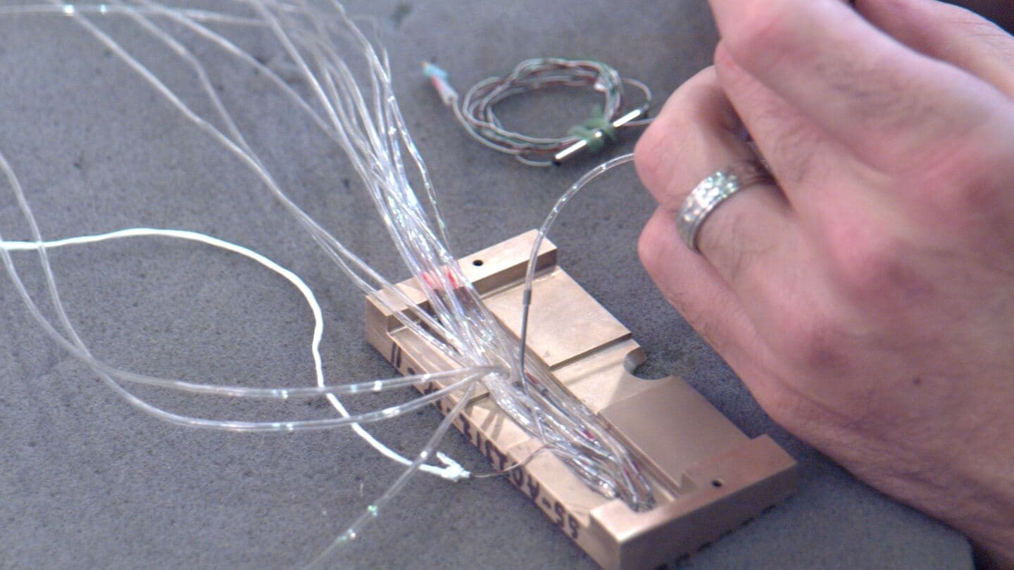 Hands routing fine fiber and wire leads on a test fixture
