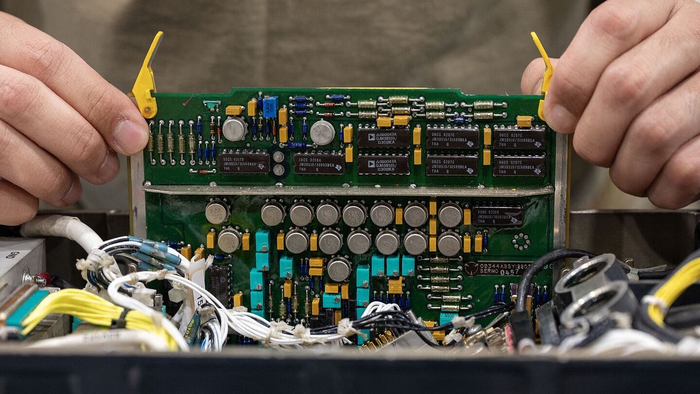 Hands holding an avionics circuit card above a repair bench