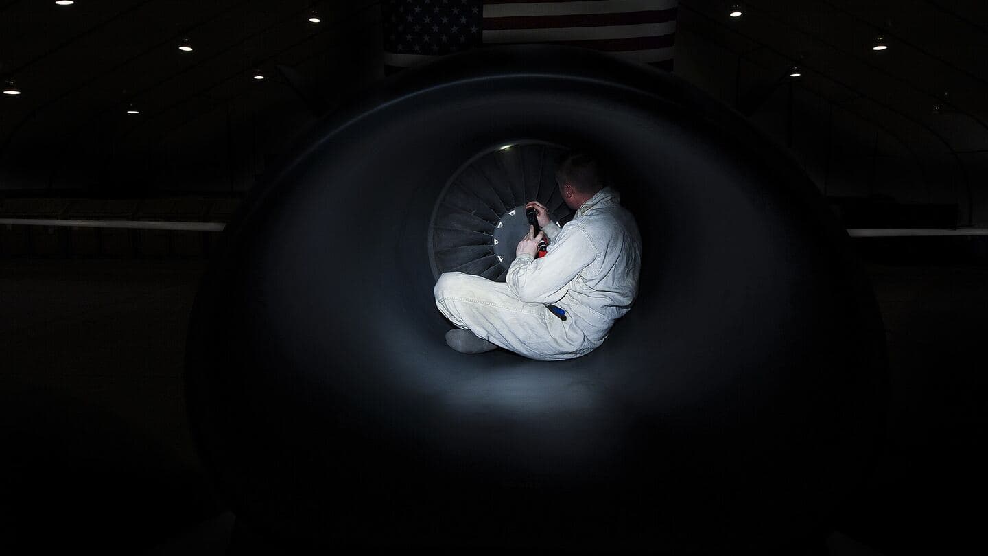 A technician in white coveralls inspecting inside a jet engine intake
