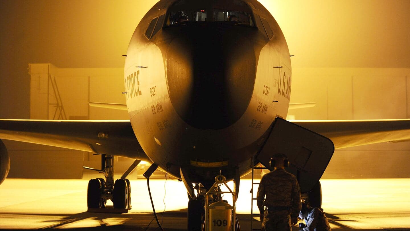 Airmen at the nose of a KC-135 tanker reviewing a technical order under floodlights at night