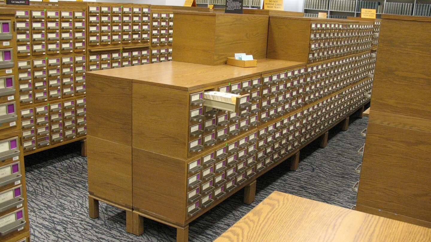 Long rows of wooden card catalog cabinets with hundreds of drawers in a library reading room