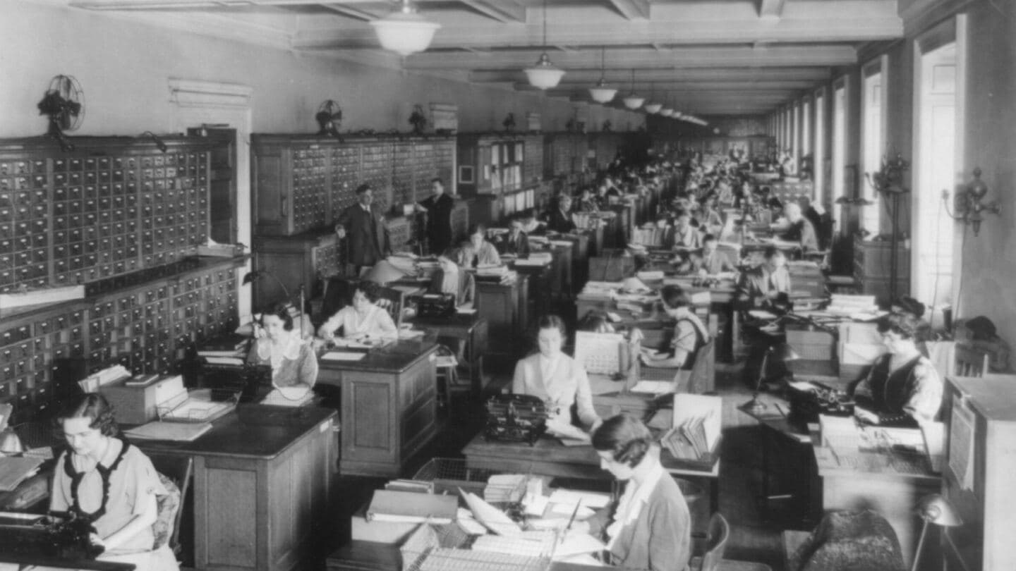 A long office of Library of Congress catalogers at desks and typewriters beside walls of card drawers