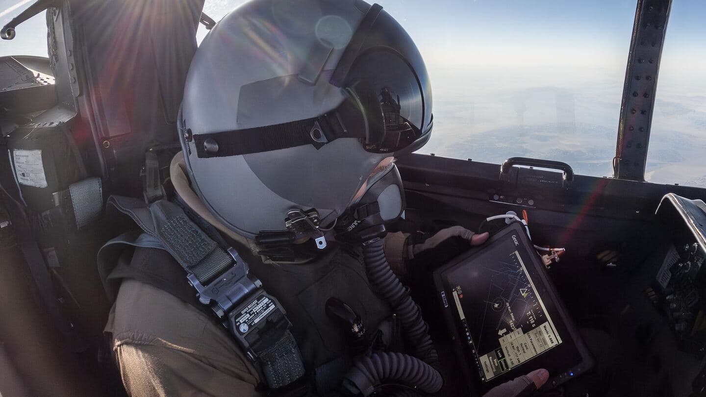 A crew member in a flight helmet holding a tablet in the cockpit
