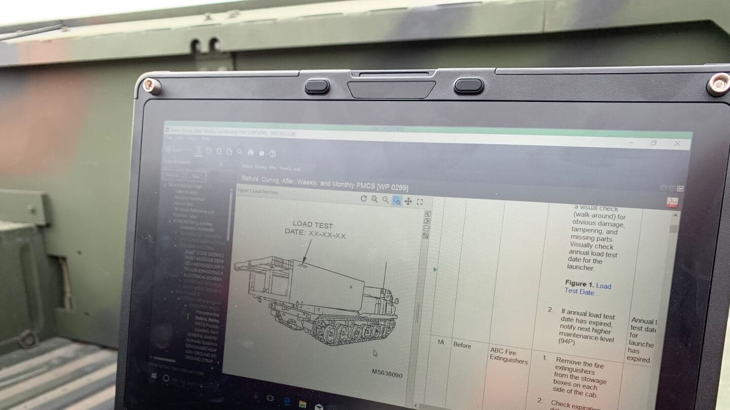 Rugged laptop on a military vehicle showing an interactive technical manual page with a launcher illustration