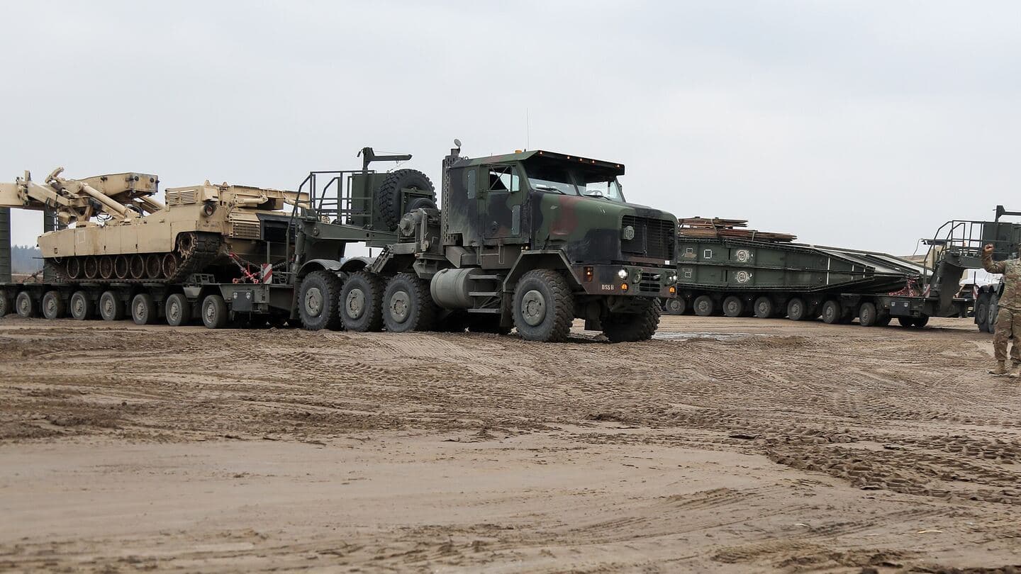 Heavy equipment transporters carrying tracked Army vehicles arrive at a muddy staging area